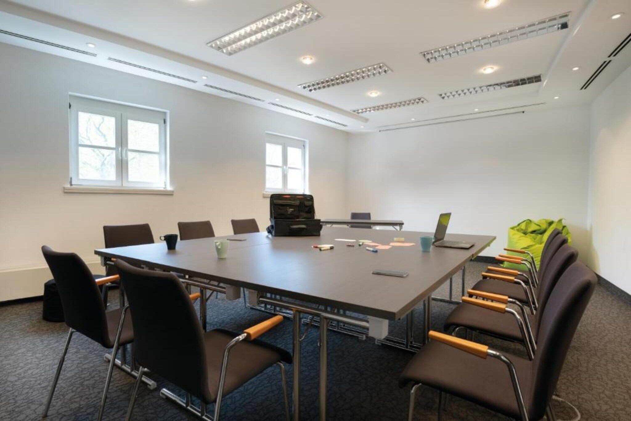 Une salle de conférence équipée d’une grande table, de chaises, d’un ordinateur portable et d’une mallette.
