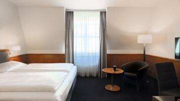 Une chambre d’hôtel avec deux lits, une petite table ronde, une chaise, un téléviseur et une fenêtre avec des rideaux.