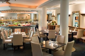 A hotel dining area with multiple tables and chairs, a bar with a counter, and a view of the kitchen area. - Hotel Leipzig Superior Double Room (Leipzig)