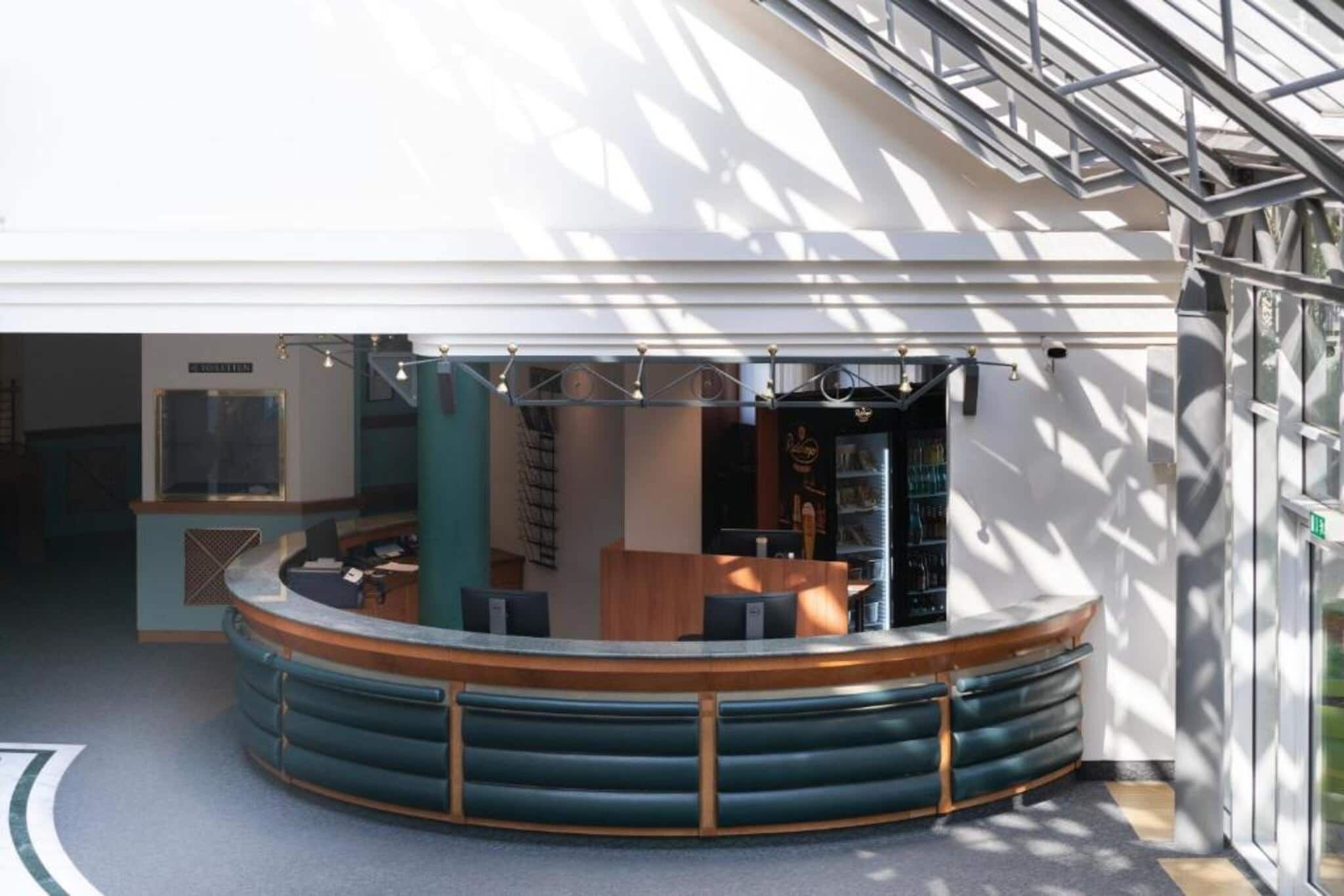 Un área de recepción moderna con un mostrador curvo, asientos y una escalera al fondo.