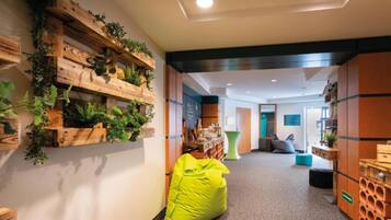 A hallway with a wooden wall adorned with greenery, a bright yellow bean bag chair, and a seating area with a blue cushion.