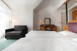 A hotel room with a bed, a desk, a chair, and a lamp.