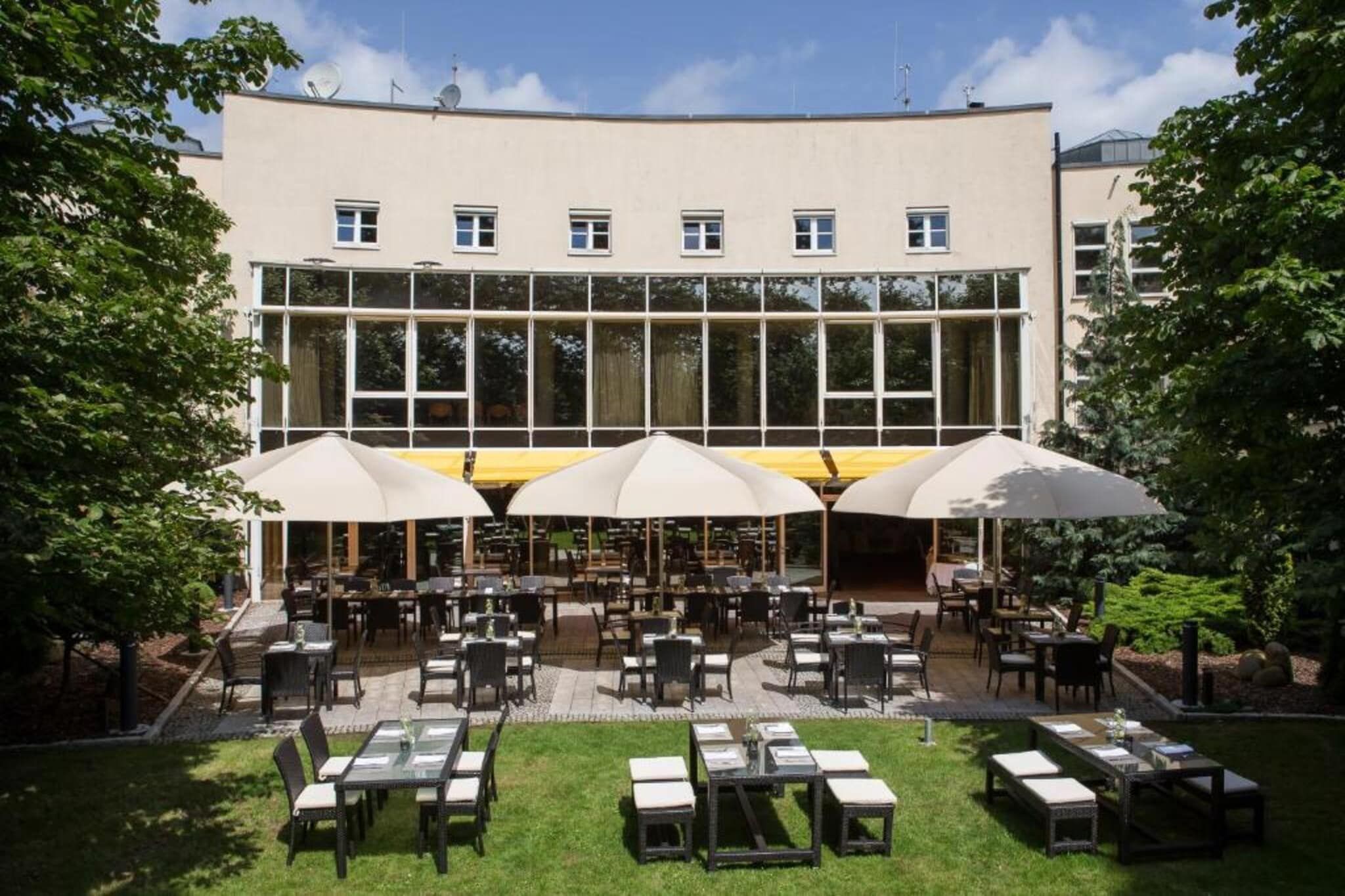 An outdoor dining area with tables and umbrellas, surrounded by a building with large windows.