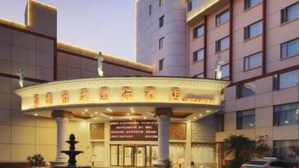 A hotel entrance with a fountain, a curved canopy, and a tall building in the background. - Vienna International Hotel Shanghai Jiaotong Unive (Shanghai)