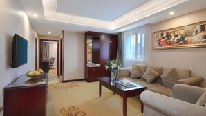 Habitación de hotel con sofá, mesa de centro, televisor y un cuadro en la pared.