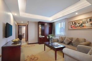 A hotel room with a sofa, a coffee table, a TV, and a painting on the wall. - Vienna International Hotel Shanghai Jiaotong Unive (Shanghai)