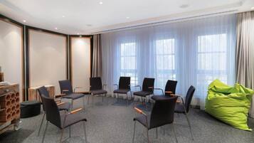 Une salle de conférence avec des chaises disposées en cercle, un pouf vert en forme de haricot et un meuble de rangement dont le motif rappelle celui d’un mur en briques.