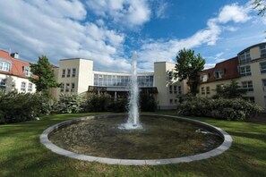 Ein Innenhof mit einem zentralen Brunnen, umgeben von Gebäuden mit zahlreichen Fenstern und blauem Himmel.