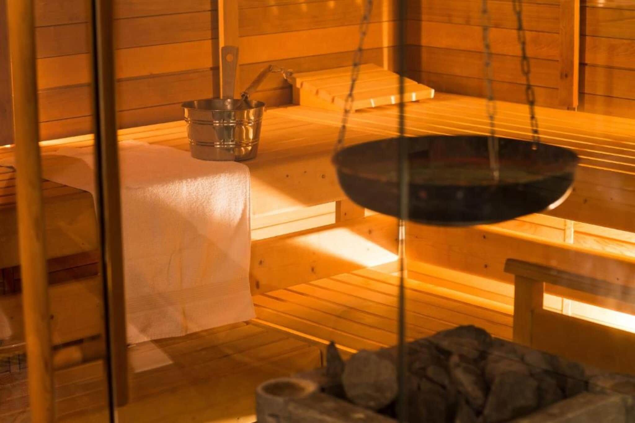 Une salle de sauna avec des bancs en bois, un grand récipient noir suspendu et un petit contenant en métal.