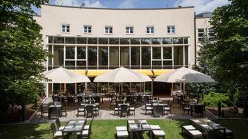 Un espace de restauration en plein air, avec des tables et des parasols, entouré d’un bâtiment doté de grandes fenêtres.