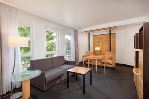 A hotel room with a sofa, a small table, a dining table with chairs, a lamp, and a wardrobe.