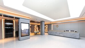 Un moderno vestíbulo de hotel con una recepción, una pantalla digital, una zona de estar y una estantería.