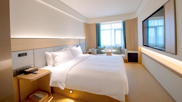 Habitación de hotel con una cama grande, mesitas de noche, un escritorio, una silla, un televisor y una ventana con cortinas.