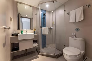 Et moderne badeværelse med bruseniche, toilet og håndvask med spejl over.