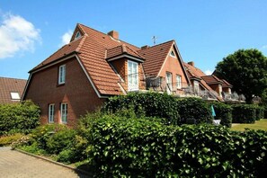 A two-story brick house with a sloped roof, a visible chimney, and a well-maintained garden with hedges. - Lüttmarsch 13, Holiday Apartment 2 (Wyk auf Föhr)
