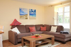 A living room with a brown sofa, a wooden coffee table, and two beach-themed wall art pieces. - Lüttmarsch 13, Holiday Apartment 2 (Wyk auf Föhr)