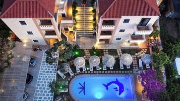 Un hotel de varios pisos con piscina, mobiliario exterior y una entrada bien iluminada.