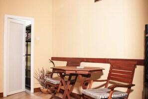 Una habitación con una mesa de madera, dos sillas, una puerta blanca y una estantería con objetos.