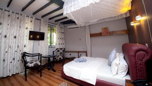 Ein Schlafzimmer mit einem Bett, einem Sessel, einem kleinen Tisch, einem Fernseher und einem Fenster mit Vorhängen.