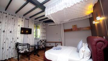 A bedroom with a bed, a chair, a small table, a TV, and a window with curtains.