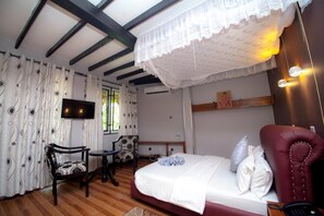 Un dormitorio con cama, una silla, una mesita, un televisor y una ventana con cortinas.