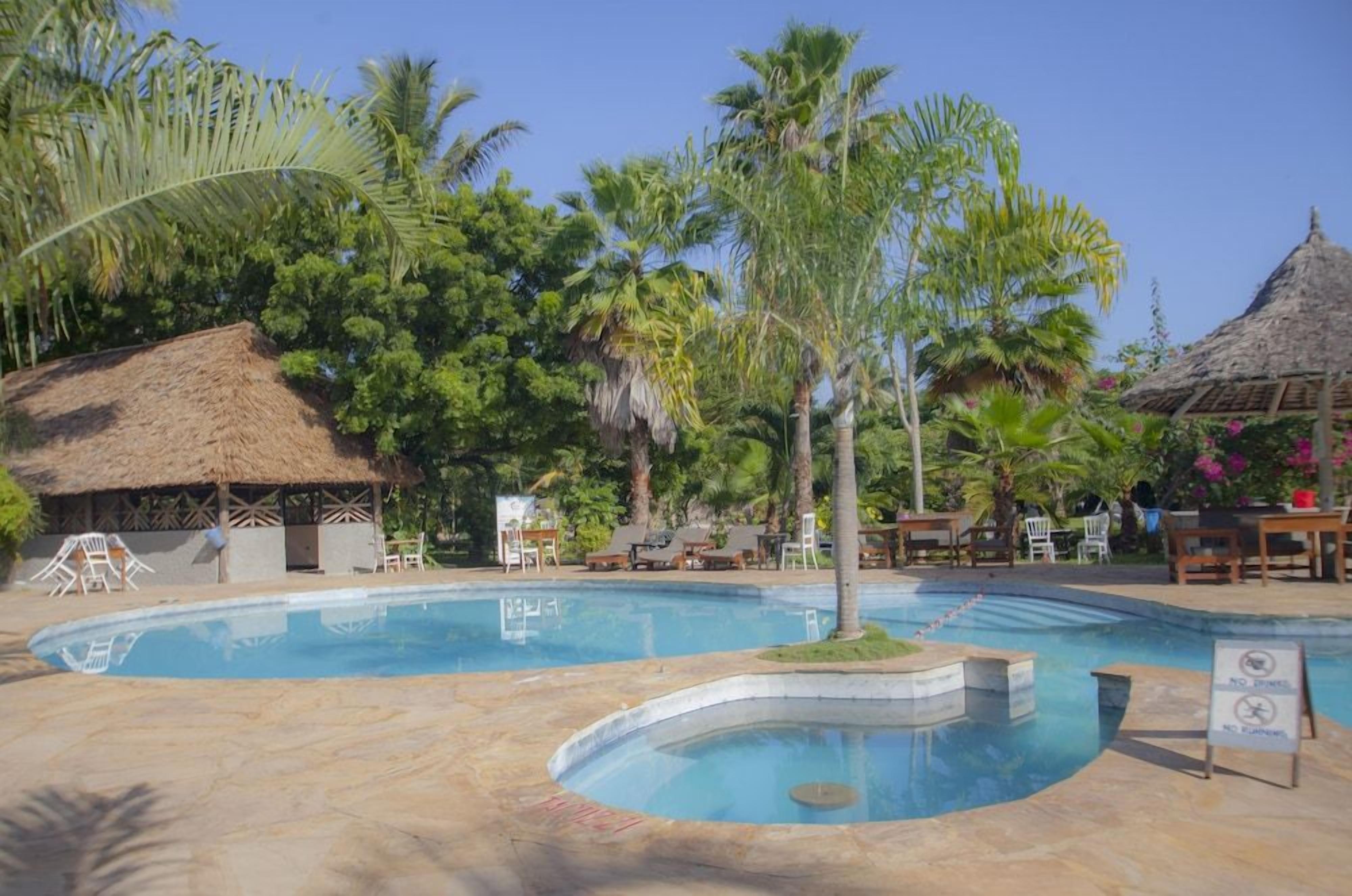 A pool area with lounge chairs, a thatched-roof structure, and tropical vegetation.