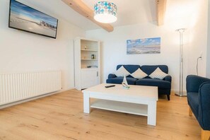 A living room with a white coffee table, a blue sofa, a white cabinet, and a painting on the wall. - Holiday apartment 2 "Hooge" (ID 471) (Tating)