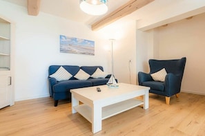 A living room with a sofa, a chair, a coffee table, and a painting on the wall. - Holiday apartment 2 "Hooge" (ID 471) (Tating)