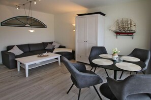 Uma sala de estar moderna com sofá, mesa de centro, mesa de jantar com cadeiras e um armário.