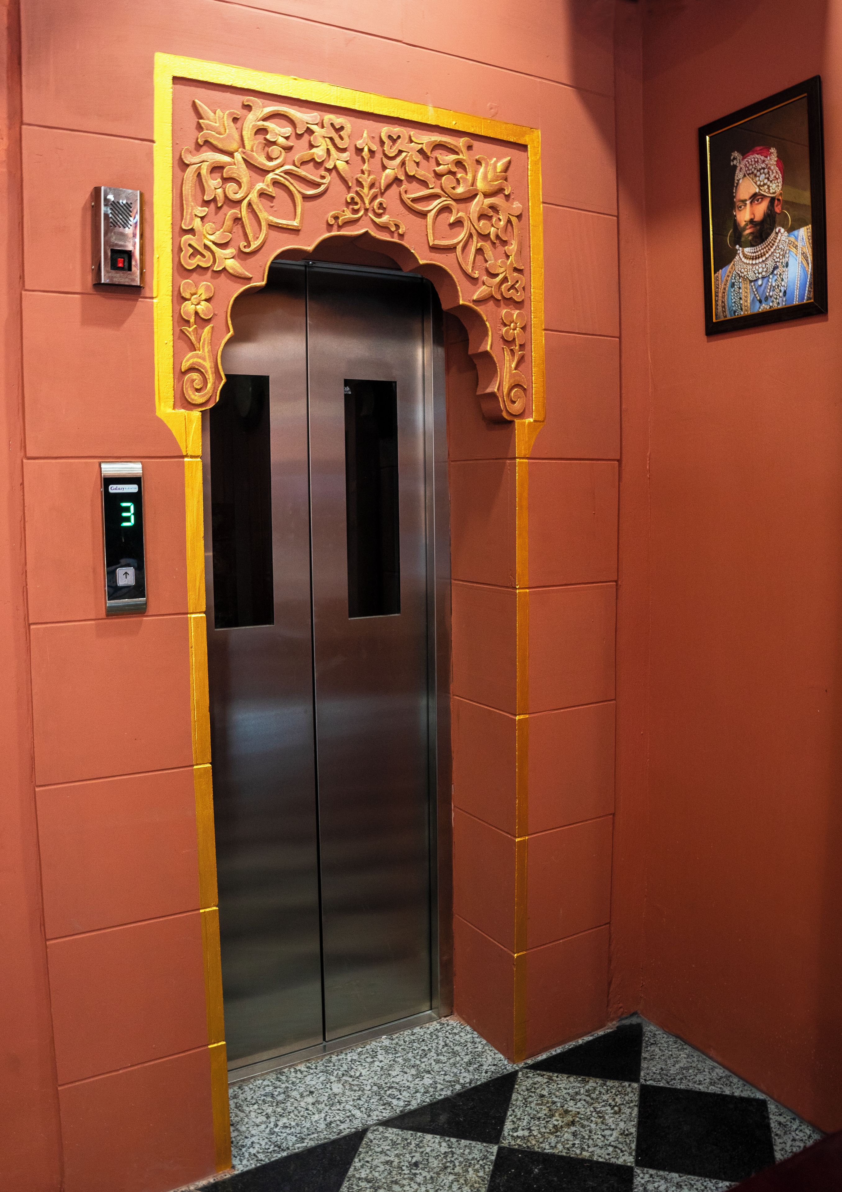 Um elevador com visor digital, arco decorativo e piso estampado.