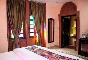 Habitación de hotel con cama, cortinas, un espejo, una puerta y una pequeña mesa con botellas.
