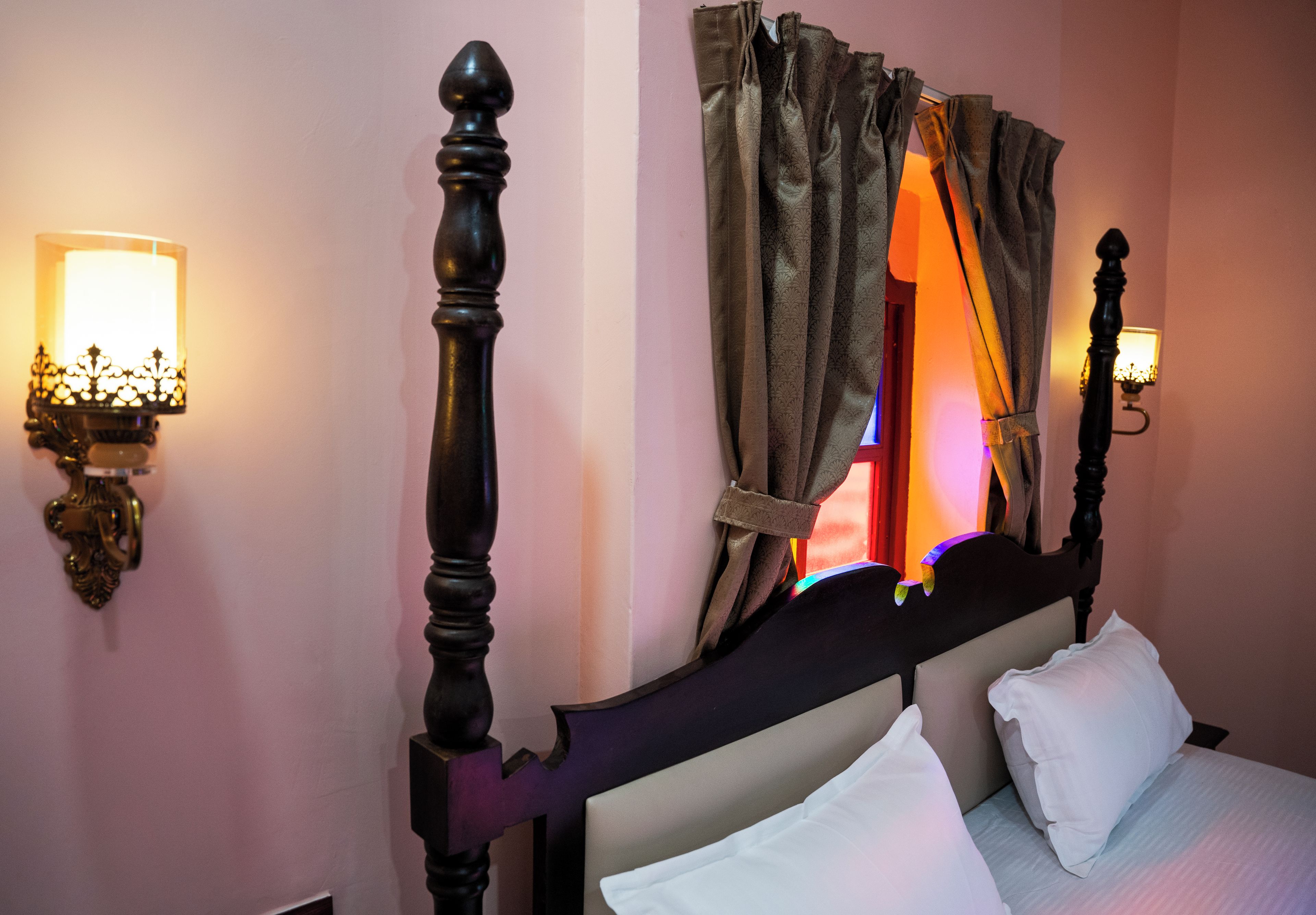 Una cama con cabecera, dos lámparas de pared y un ventanal con cortinas.