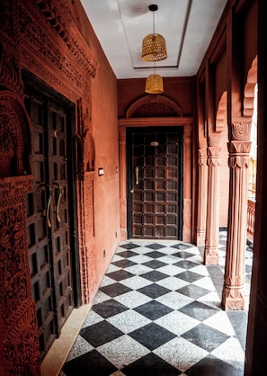 A hallway with ornate doors, a checkered floor, and a hanging light fixture.