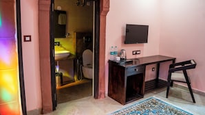 A room with a wooden desk, a chair, a television mounted on the wall, and a bathroom visible through an open door. - Jhalra Heritage Haveli Jodhpur (Jodhpur)