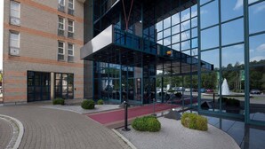 A modern building with a glass facade, a brick lower section, and a paved entrance area with a red carpet and small bushes. - Hotel Nürnberg- Superior Plus Room (Nuremberg)