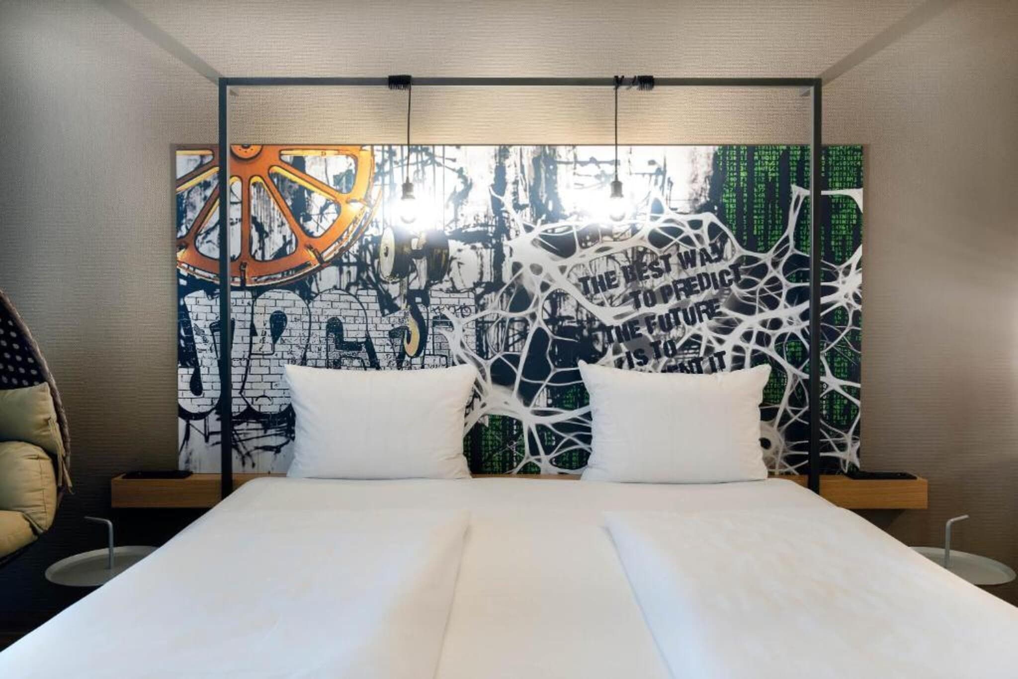 Una habitación de hotel moderna con una cama grande, dos almohadas blancas y una original pieza de arte abstracto en la pared.
