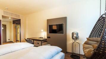 Ein Hotelzimmer mit Bett, Schreibtisch, Stuhl, Hängesessel und Fernseher.