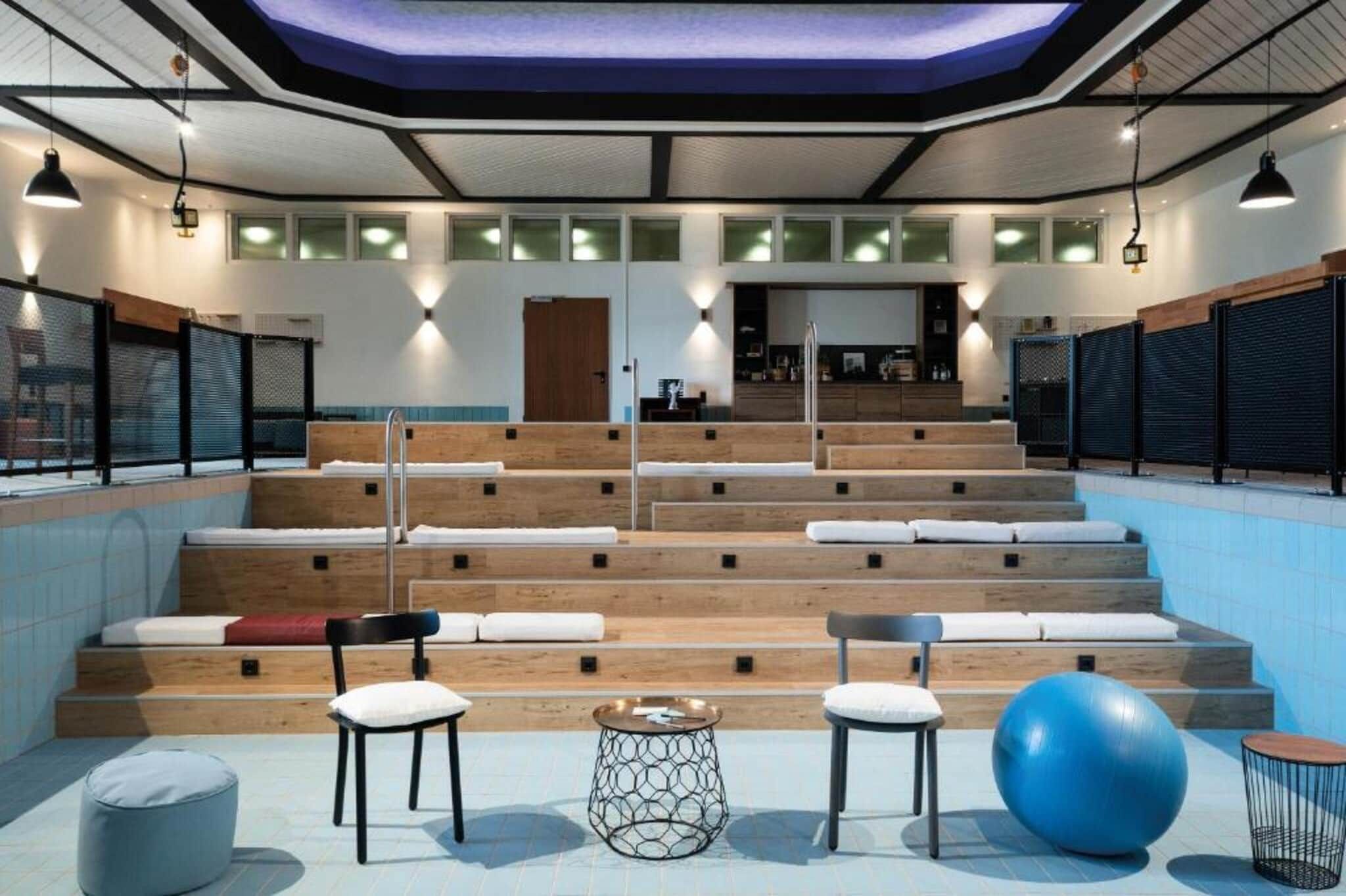 Un área moderna de piscina interior con escalones que conducen a un espacio de descanso, una pelota de ejercicios grande y una pequeña mesa redonda.