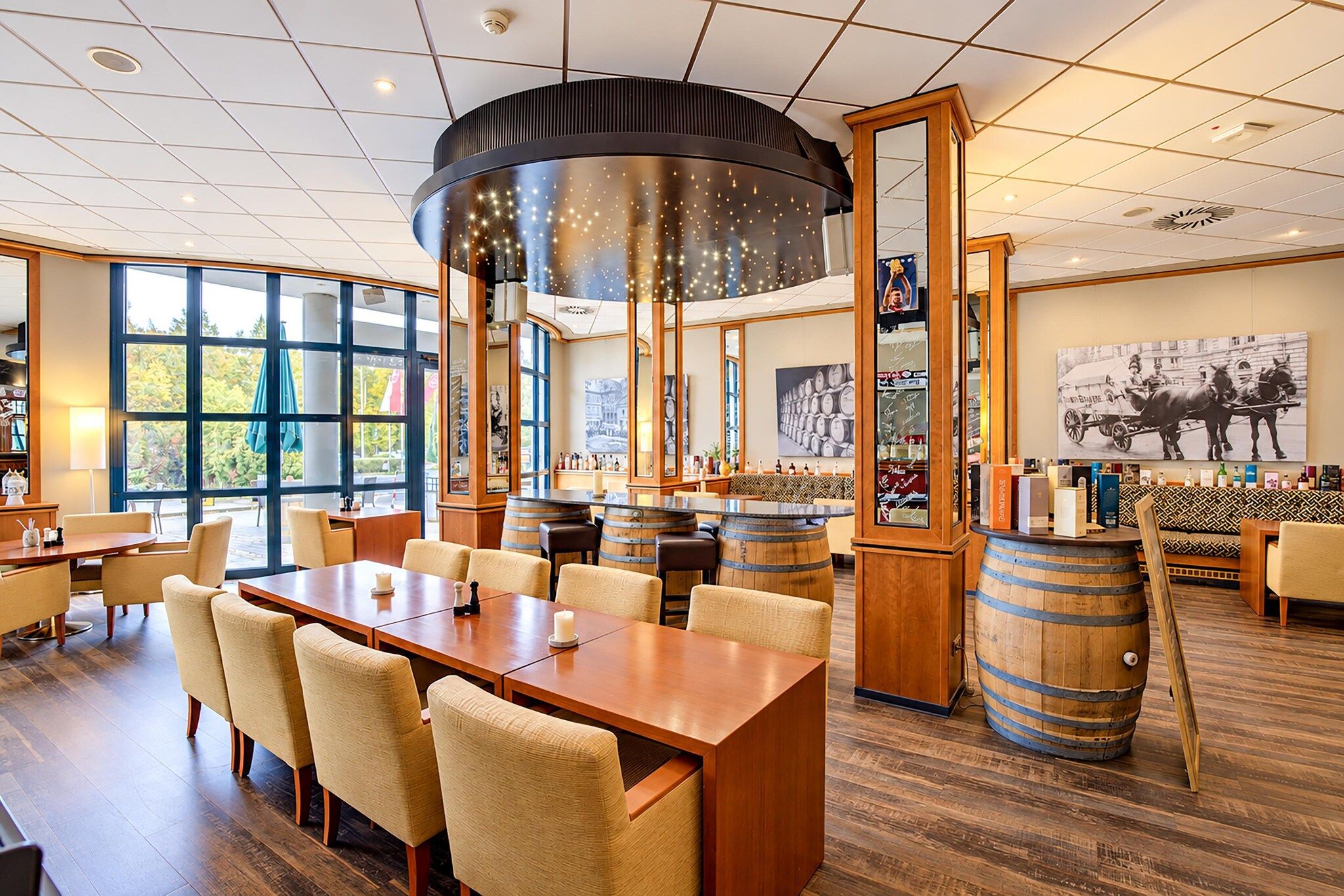 Ein Restaurantinneres mit einem langen Holztisch, gepolsterten Stühlen, einer Bar mit Flaschen und einem großen Fenster mit Blick ins Freie.