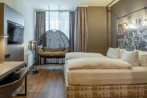 Ein Hotelzimmer mit Bett, Schreibtisch, Stuhl, Hängesessel und einem großen Fenster mit Vorhängen.