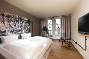 Une chambre d’hôtel avec un grand lit, un fauteuil suspendu, une télévision et une fresque représentant un paysage urbain sur le mur.
