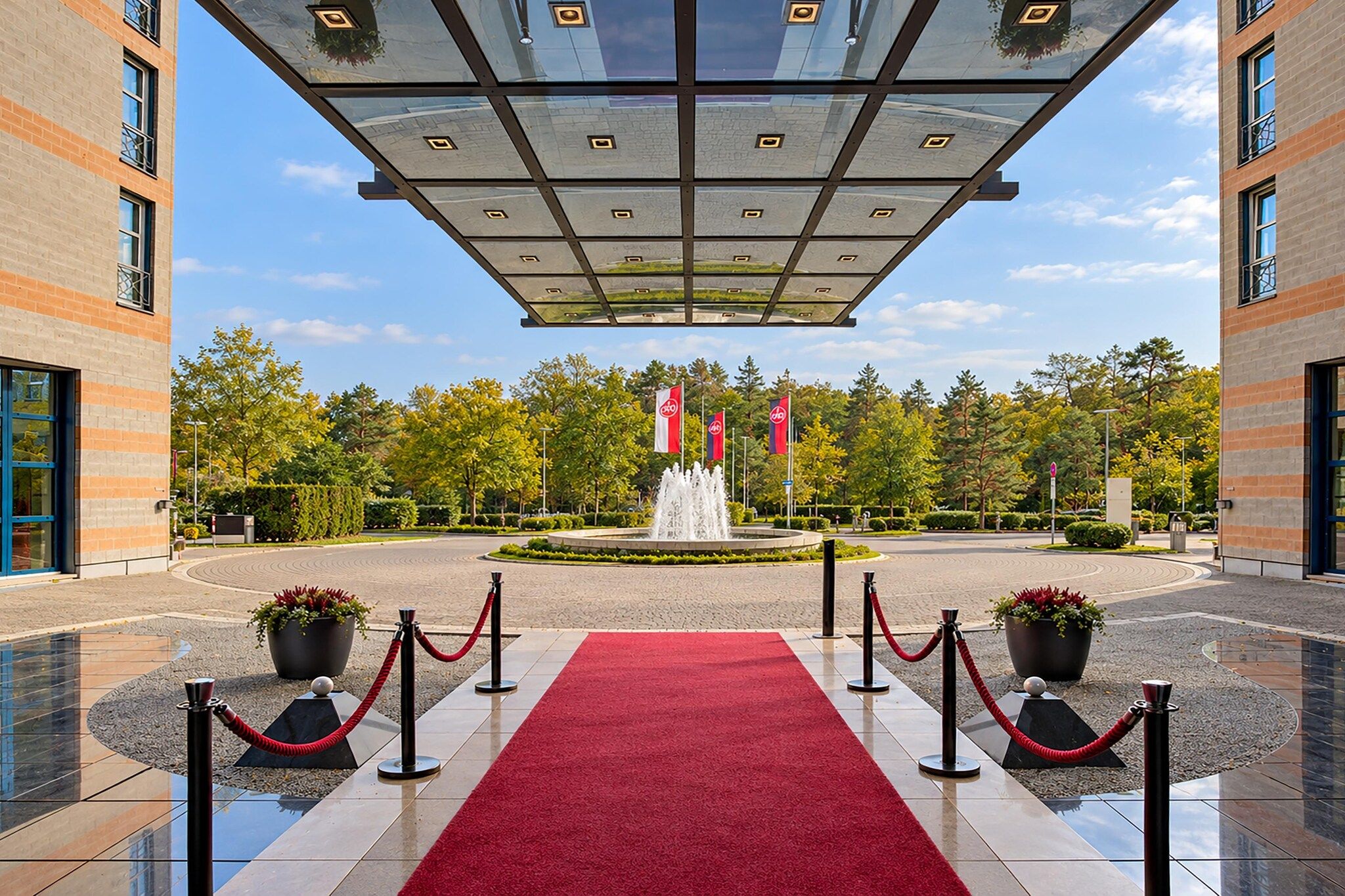 A hotel entrance with a red carpet, a fountain, and flags.