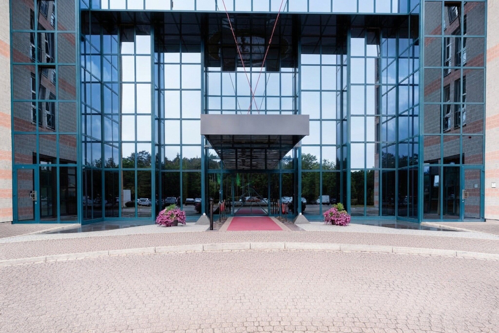 Ein modernes Gebäude mit Glasfassade, einem zentralen Eingang mit rotem Teppich und symmetrischer Gestaltung.