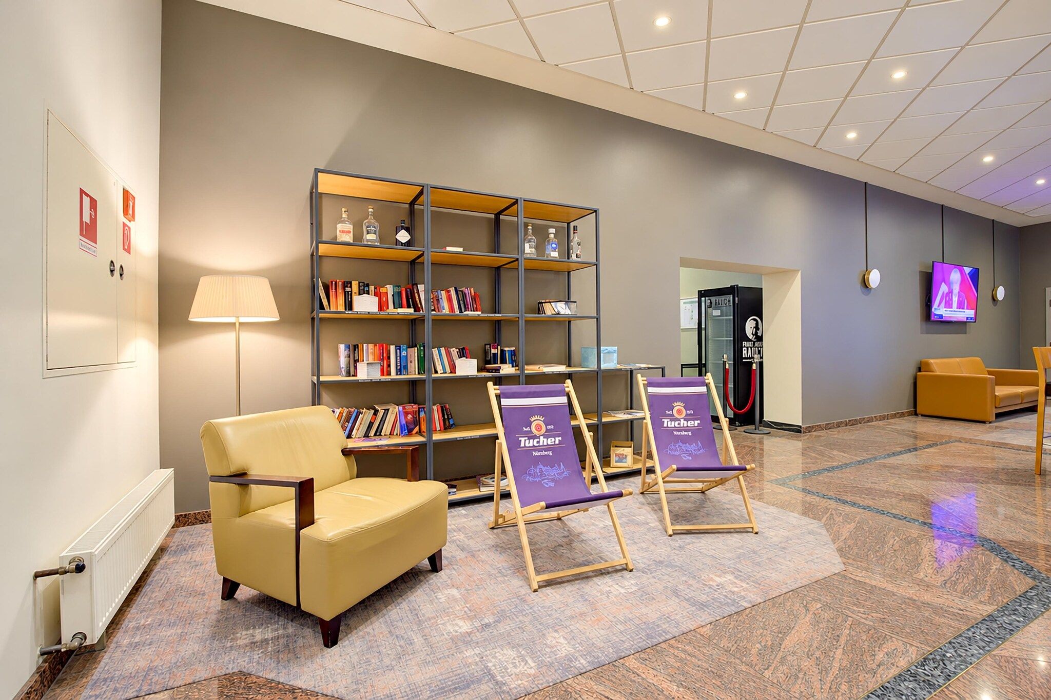 A lobby with a seating area, a bookshelf, and a television screen.