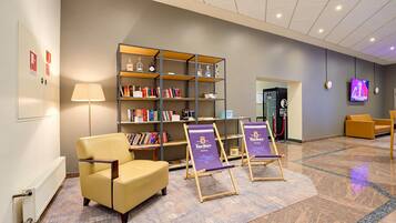 A lobby with a seating area, a bookshelf, and a television screen.