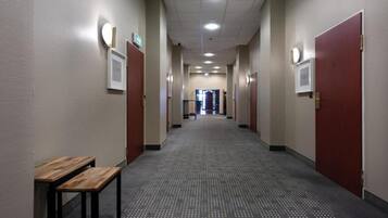 A hotel corridor with a wooden bench, doors, and a carpeted floor.