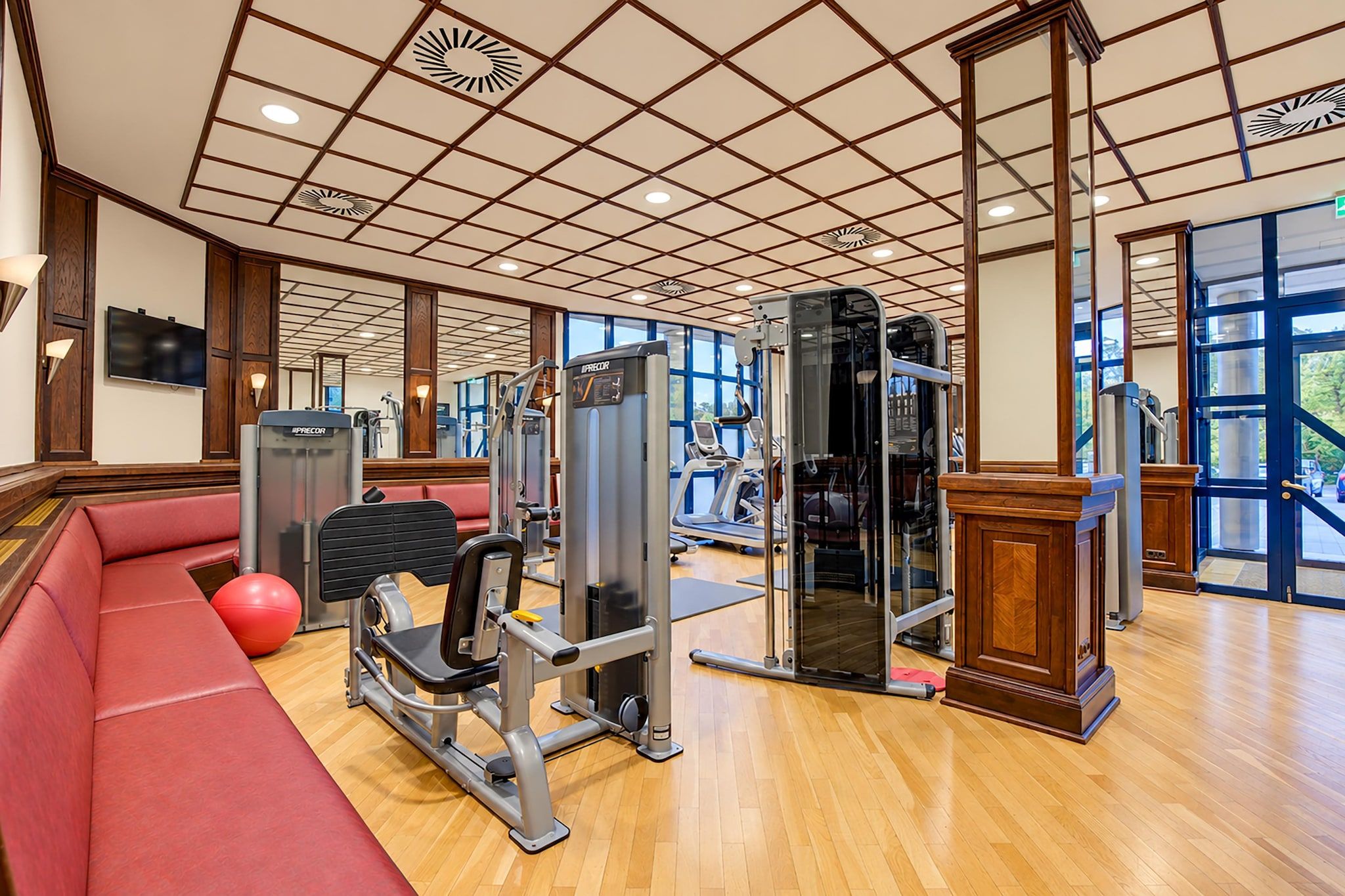 A gym with exercise equipment, a red sofa, and a television on the wall.
