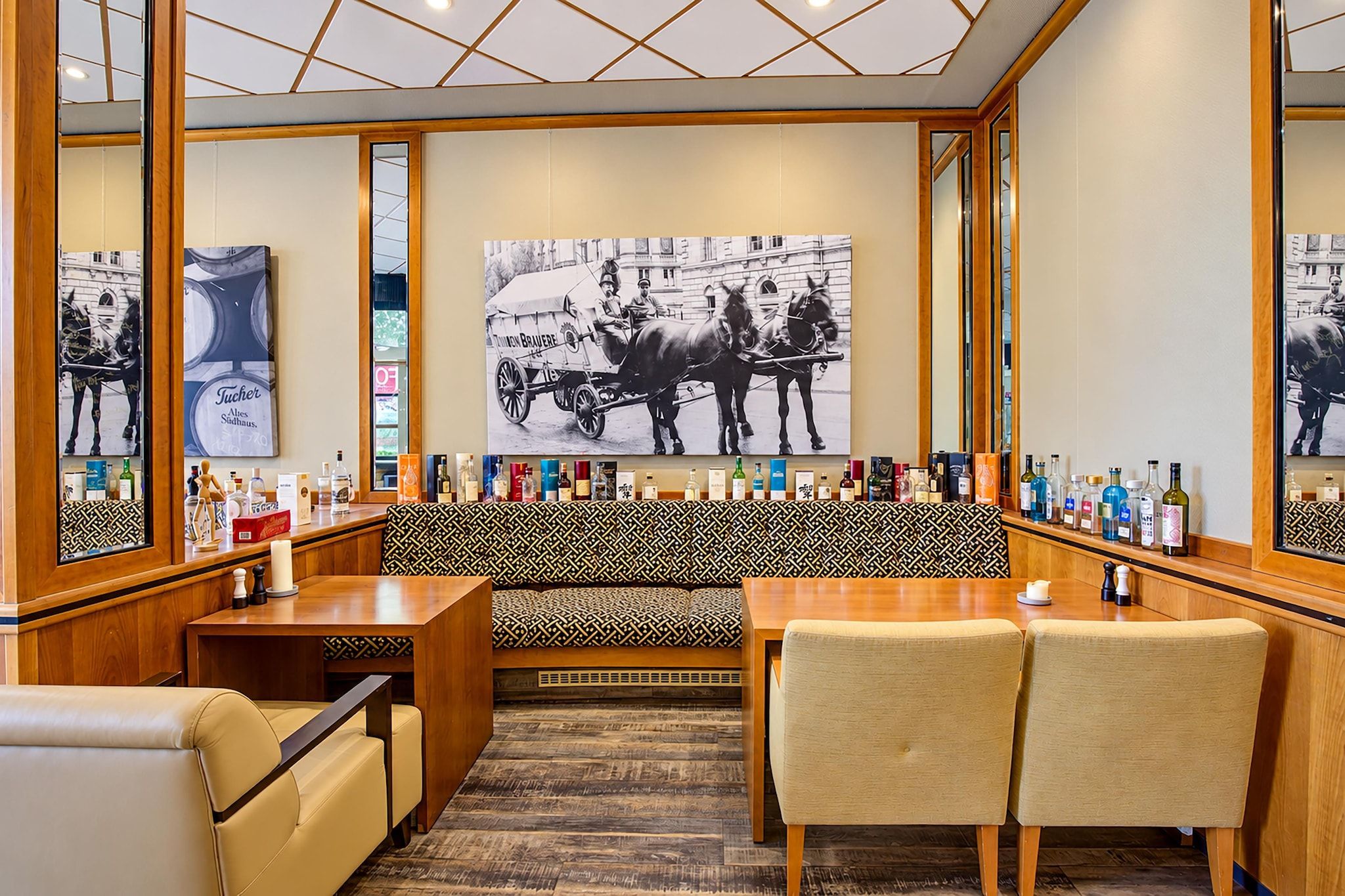 Eine Bar mit einer langen Holztheke, Sitzgelegenheiten mit gemusterten Kissen und einem großen Wandbild.