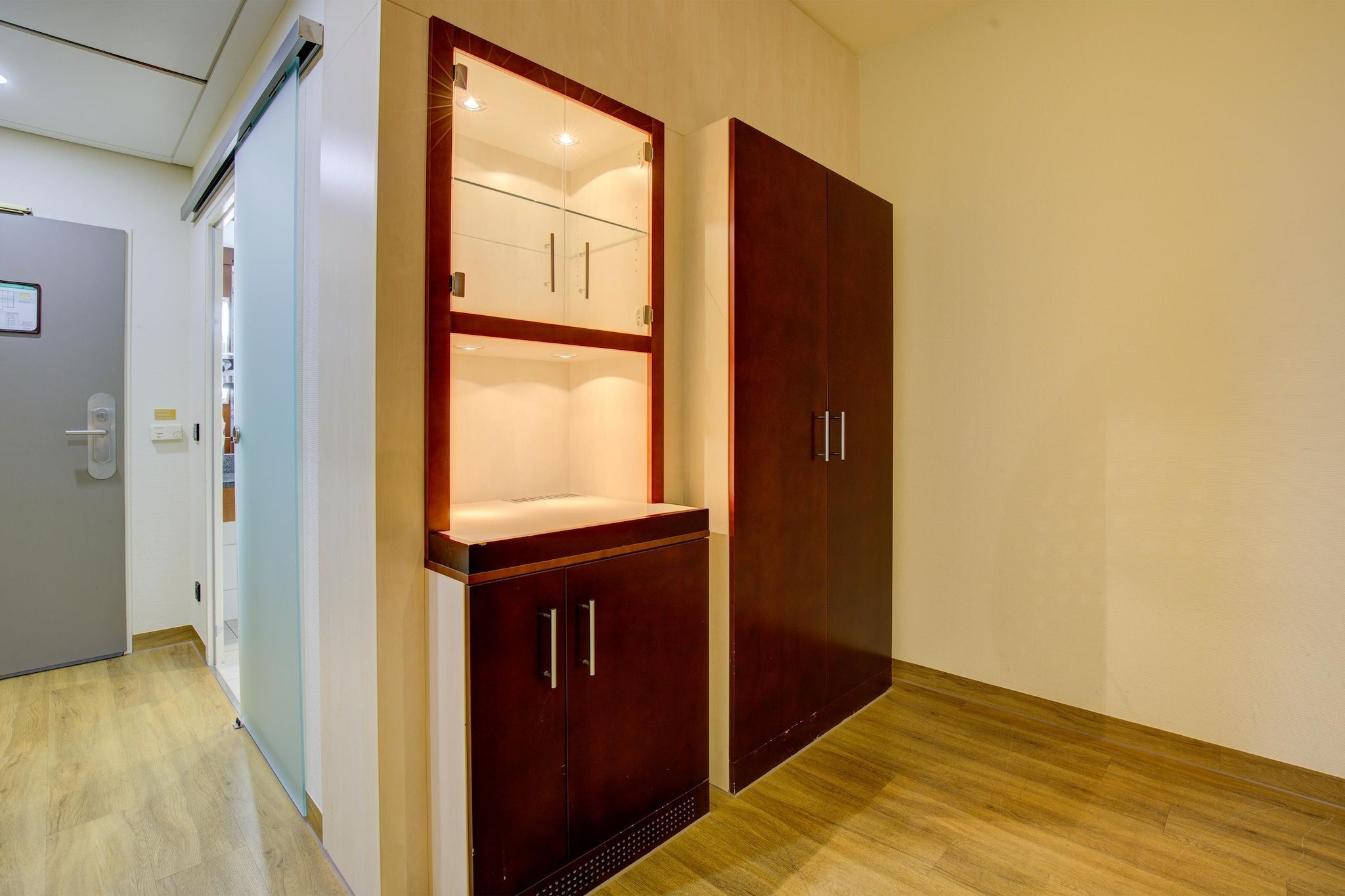 A room with a wooden wardrobe, a glass cabinet, and a door with a handle.