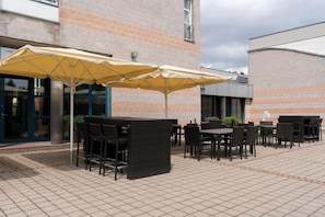 Un espace extérieur aménagé avec des tables et des chaises, des parasols, et un bâtiment en briques en arrière-plan.